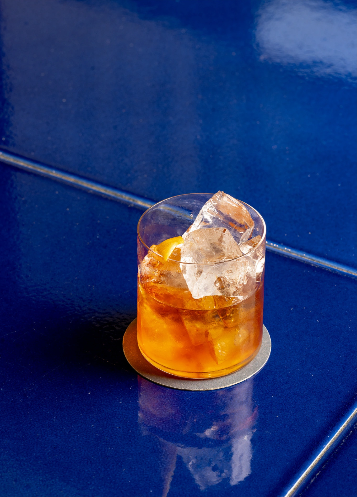 Amber cocktail with ice cube on blue background at Experimental Cocktail Club, Cotswolds