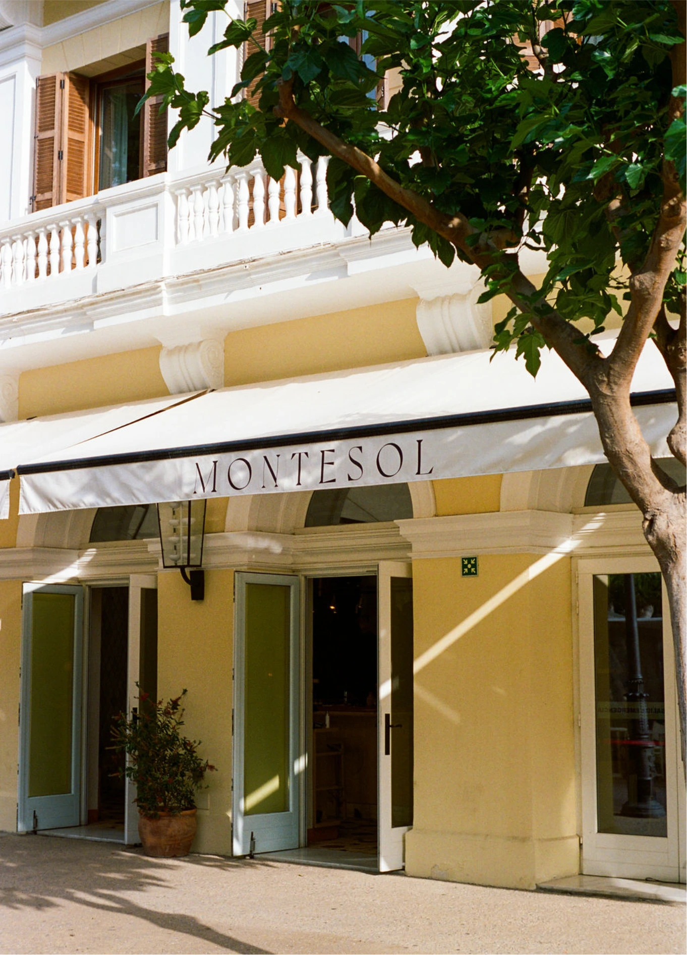 Exterior facade of Experimental Beach Ibiza, showcasing classic-style architecture with an awning and a tree in the foreground.