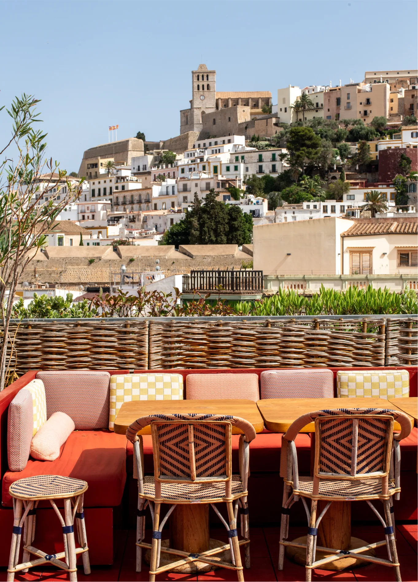 Terrace area at Experimental Beach Ibiza with colorful sofas, rattan chairs, and a panoramic view of the buildings in the background.