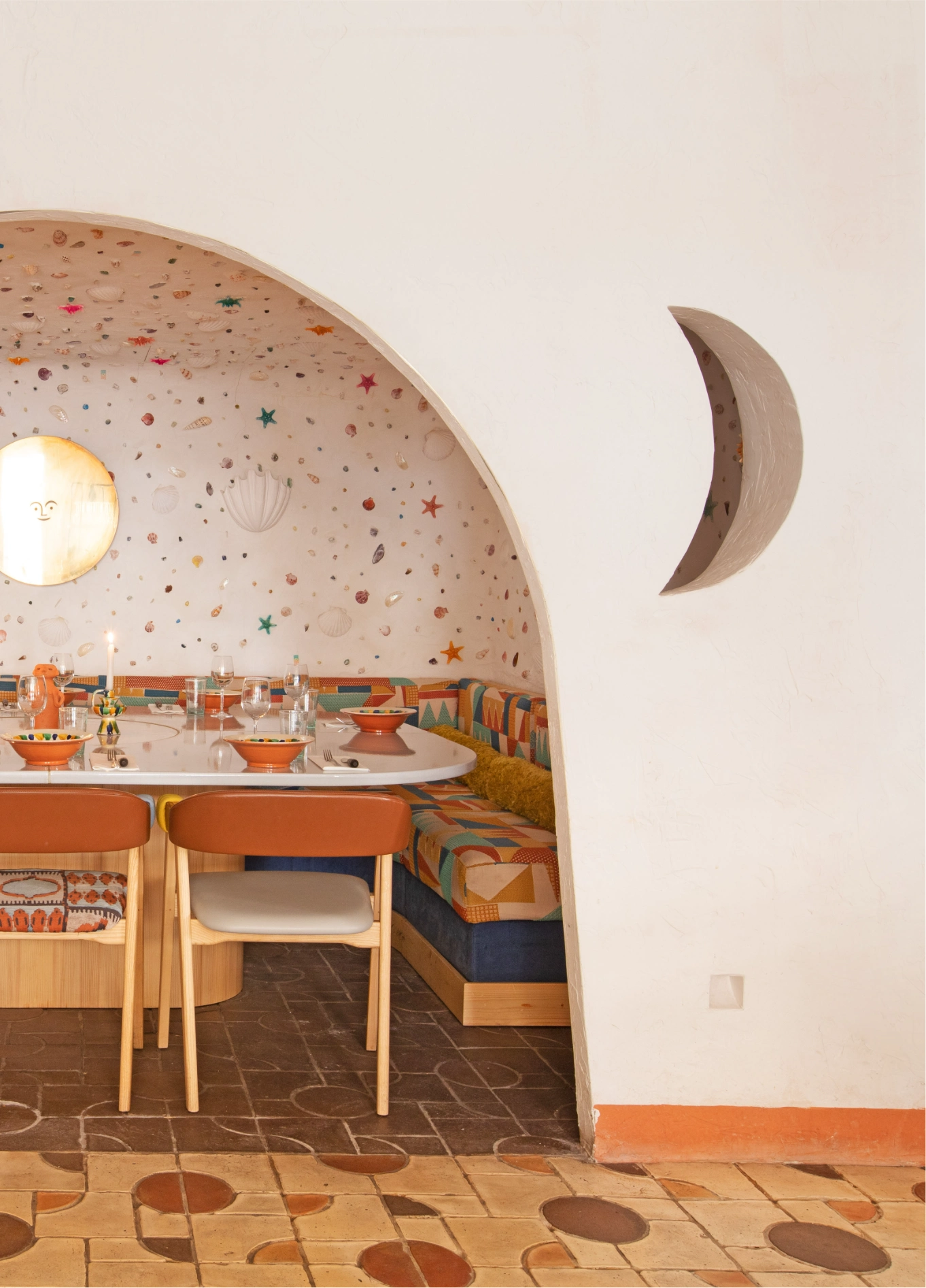 dining area viewed through an archway, featuring a moon-shaped wall decoration, tables with chairs, and a tiled floor.