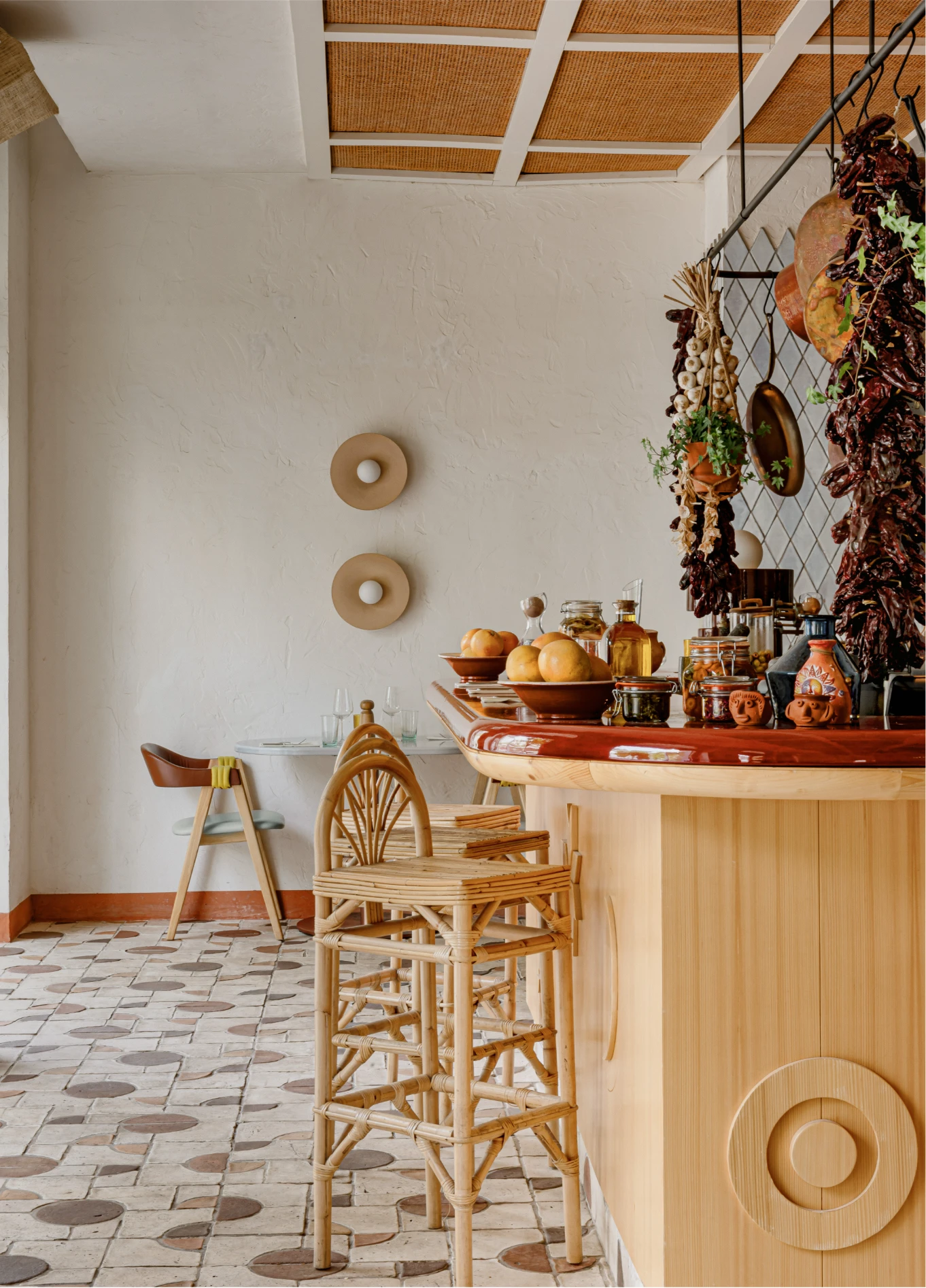 The interior of a bar with wooden counters, high stools, and varied decor hanging from the ceiling, set on a tiled floor.