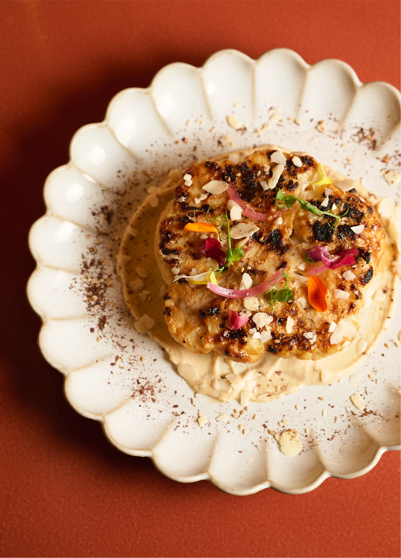 A prepared dish served on a white plate with scalloped edges, set on an orange table.