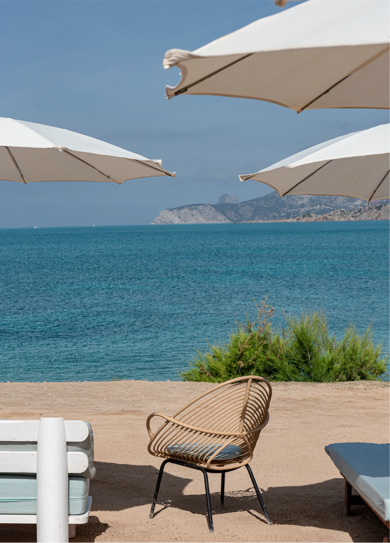 Relaxing view of the sea from a terrace equipped with white parasols and lounge chairs.