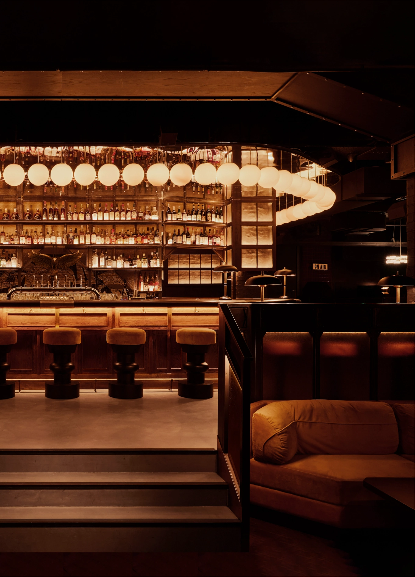 View of the interior of a stylish bar by the Experimental Group, featuring a backlit counter, bar stools, and a cozy lounge area.