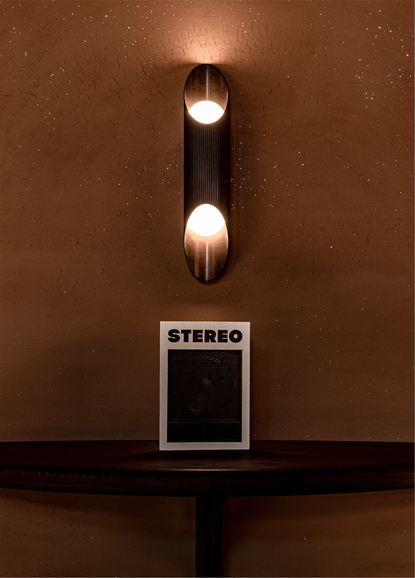 A modern wall sconce casting soft light above a small "STEREO" sign in an Experimental Group space.