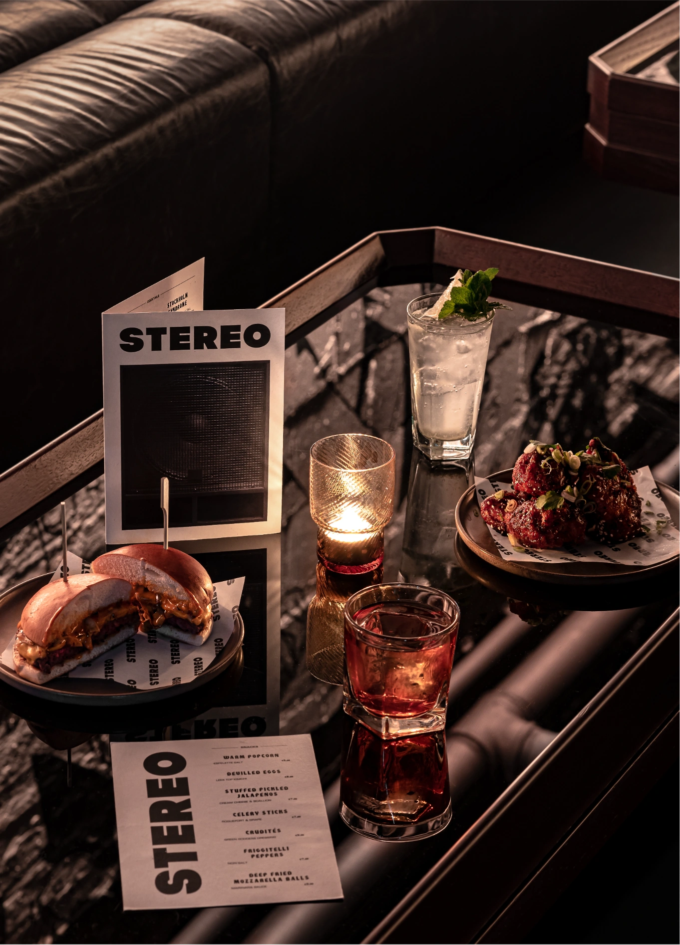 A coffee table in an Experimental Group lounge with glasses, drinks, snacks, and a menu featuring the name "STEREO".
