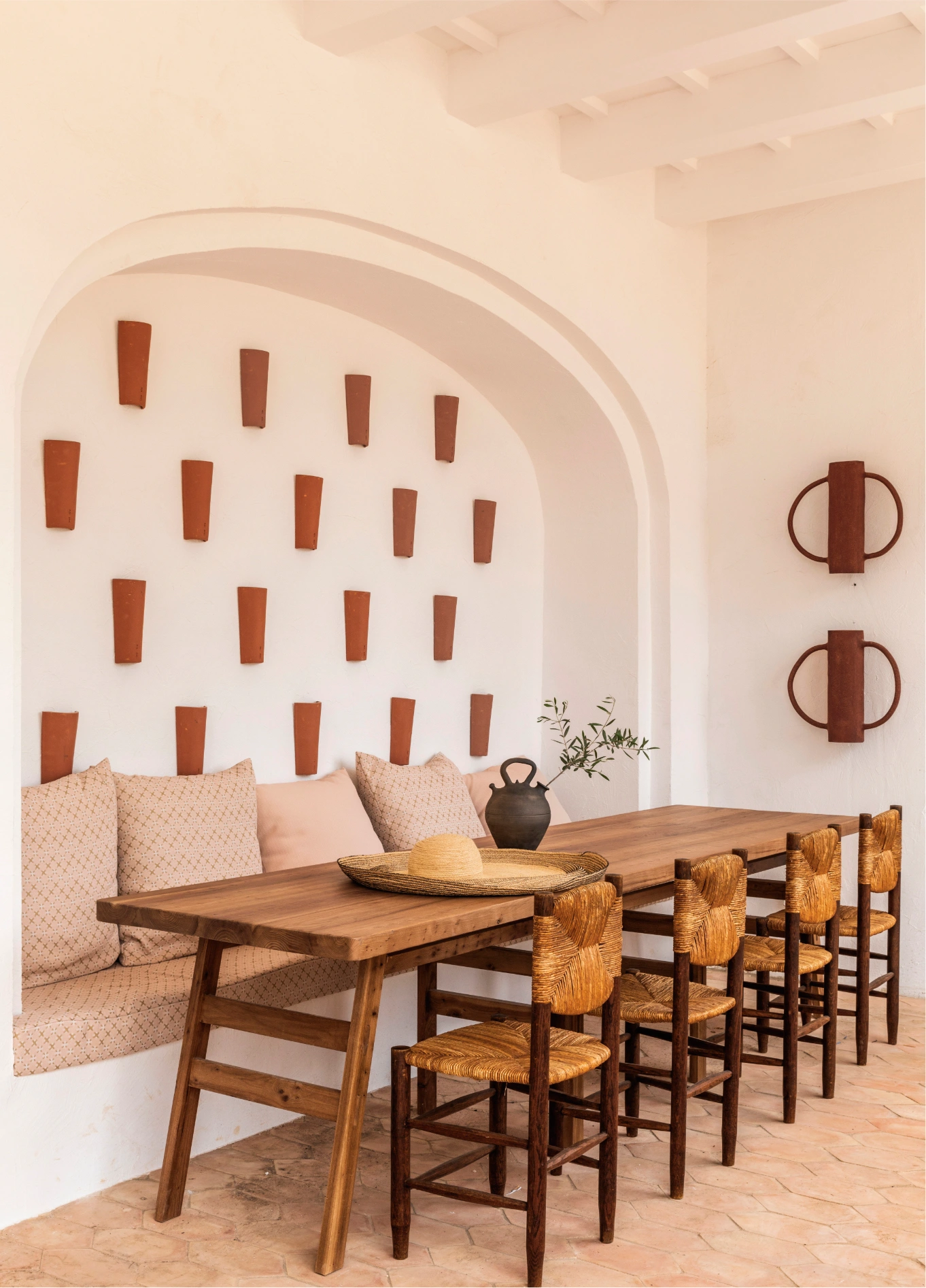 Elegant dining room at Manorca Experimental, featuring a built-in banquette, wooden chairs, and ceramic wall decor under an arch.