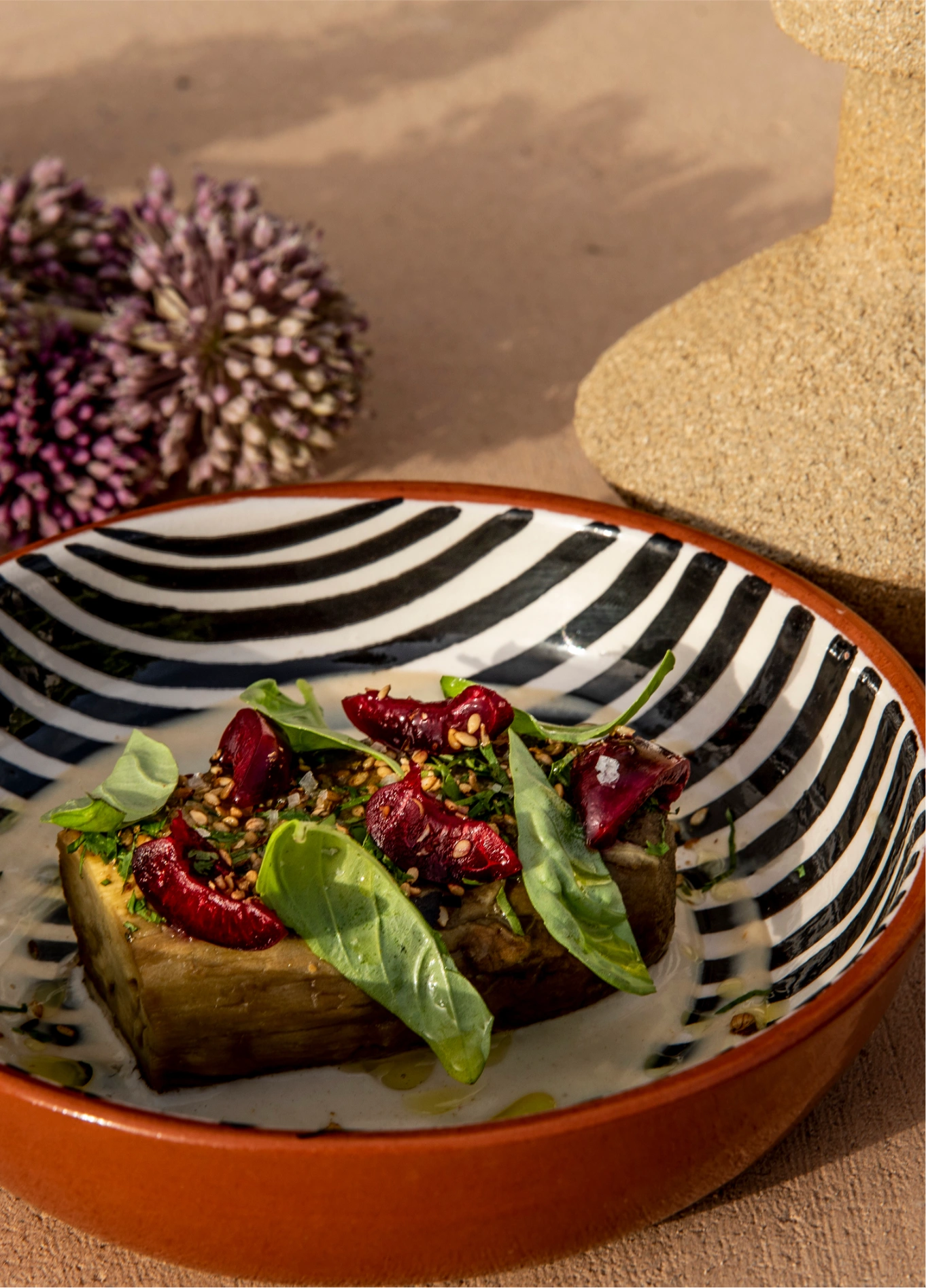 Gourmet dish served at Menorca Experimental, featuring a piece of toast topped with vegetables and fresh herbs, presented on a black and white striped patterned plate.