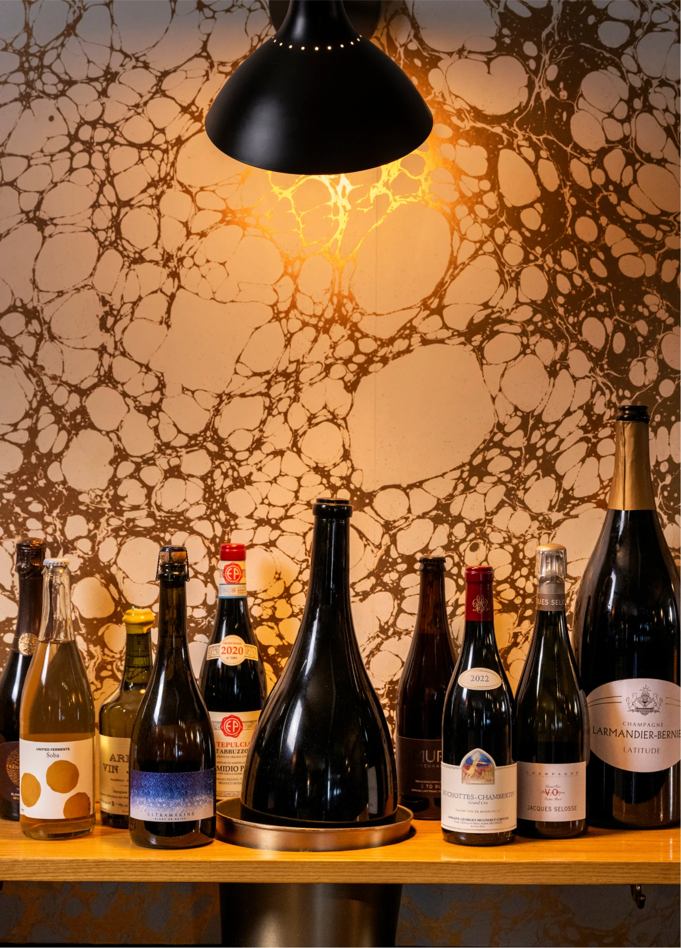 Diverse selection of wine bottles displayed on a shelf under warm lighting at La Compagnie Wine Bar.