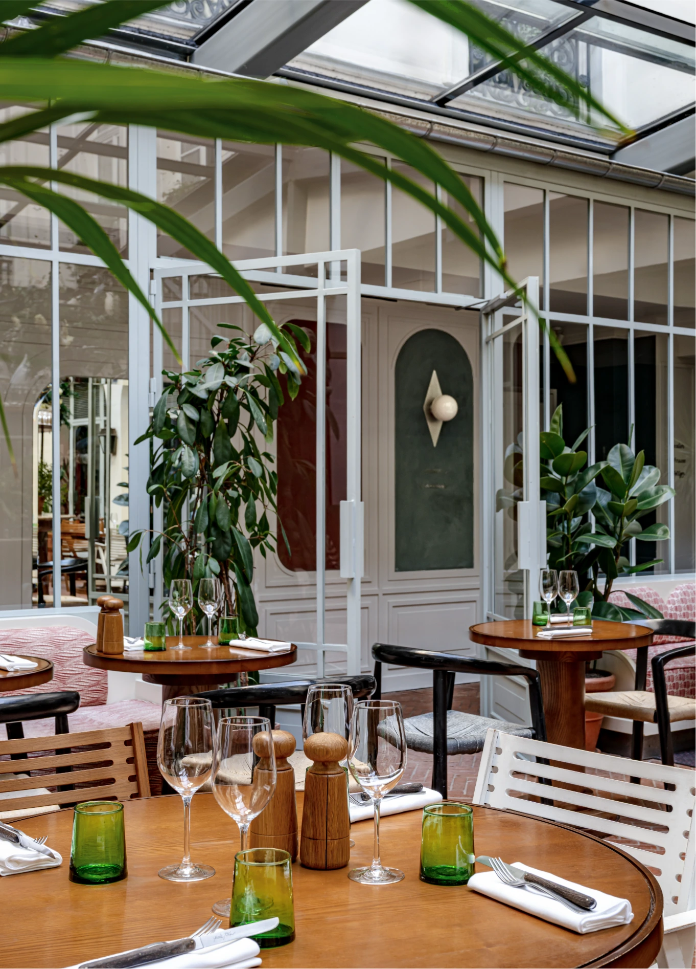 Bright dining room with glass roof, wooden tables and plants at Restaurant des Grands Boulevards, Paris