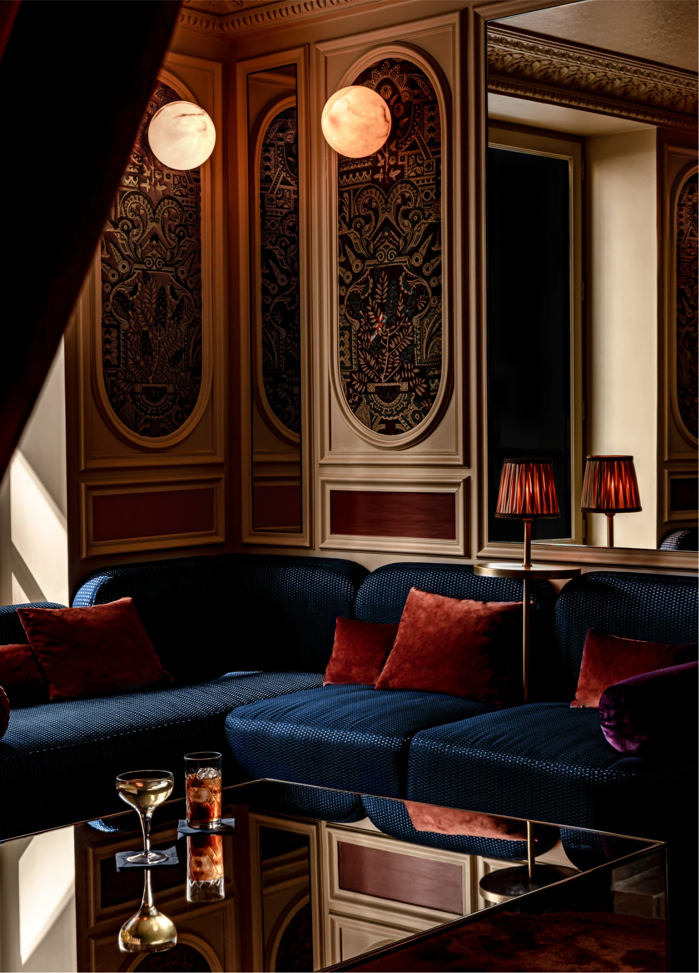 A cozy lounge area with deep blue sofas, red cushions, and dim lighting, creating a sophisticated atmosphere.