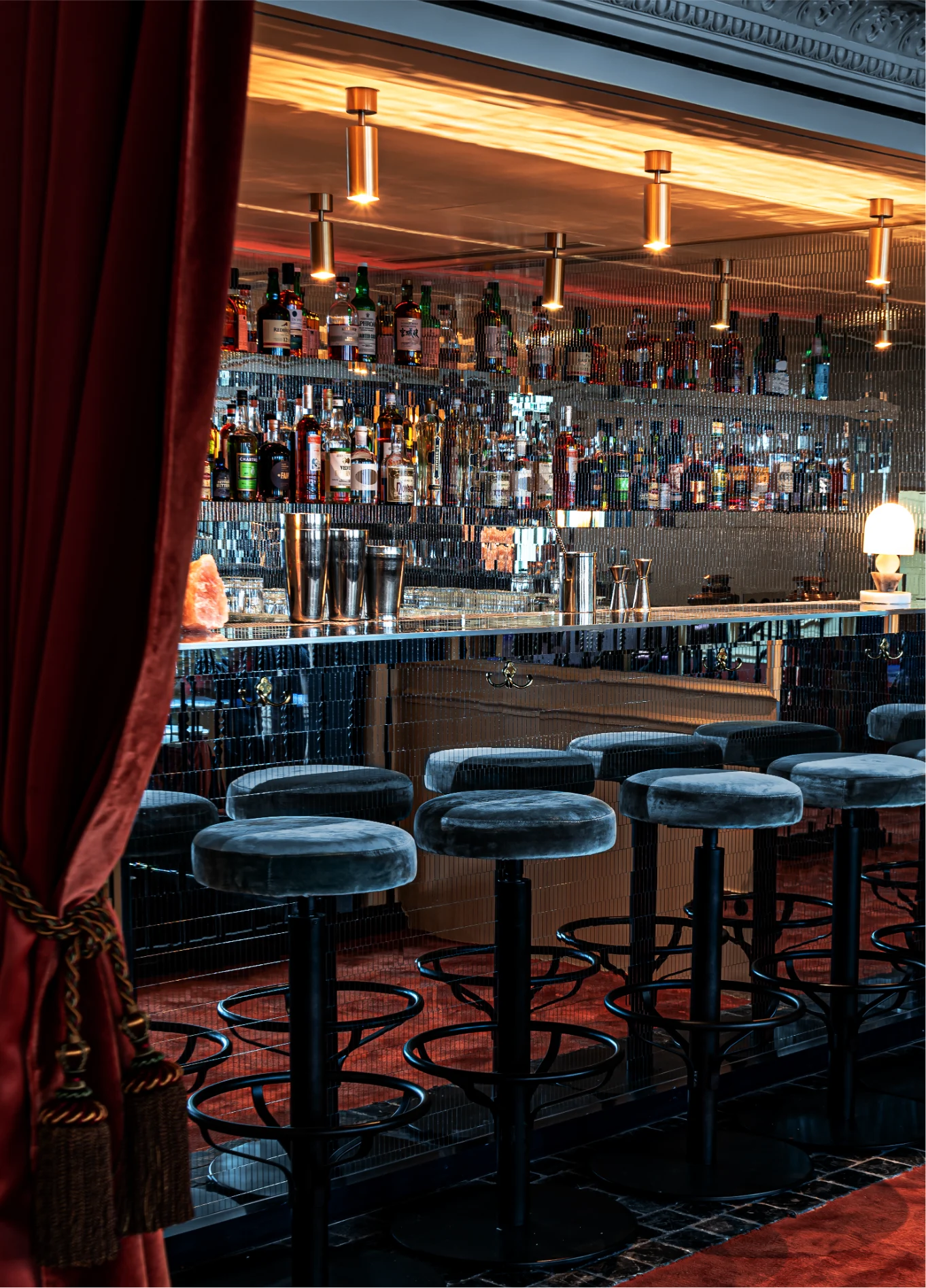 An elegant bar counter with high stools and shelves filled with bottles, highlighted by warm lighting.