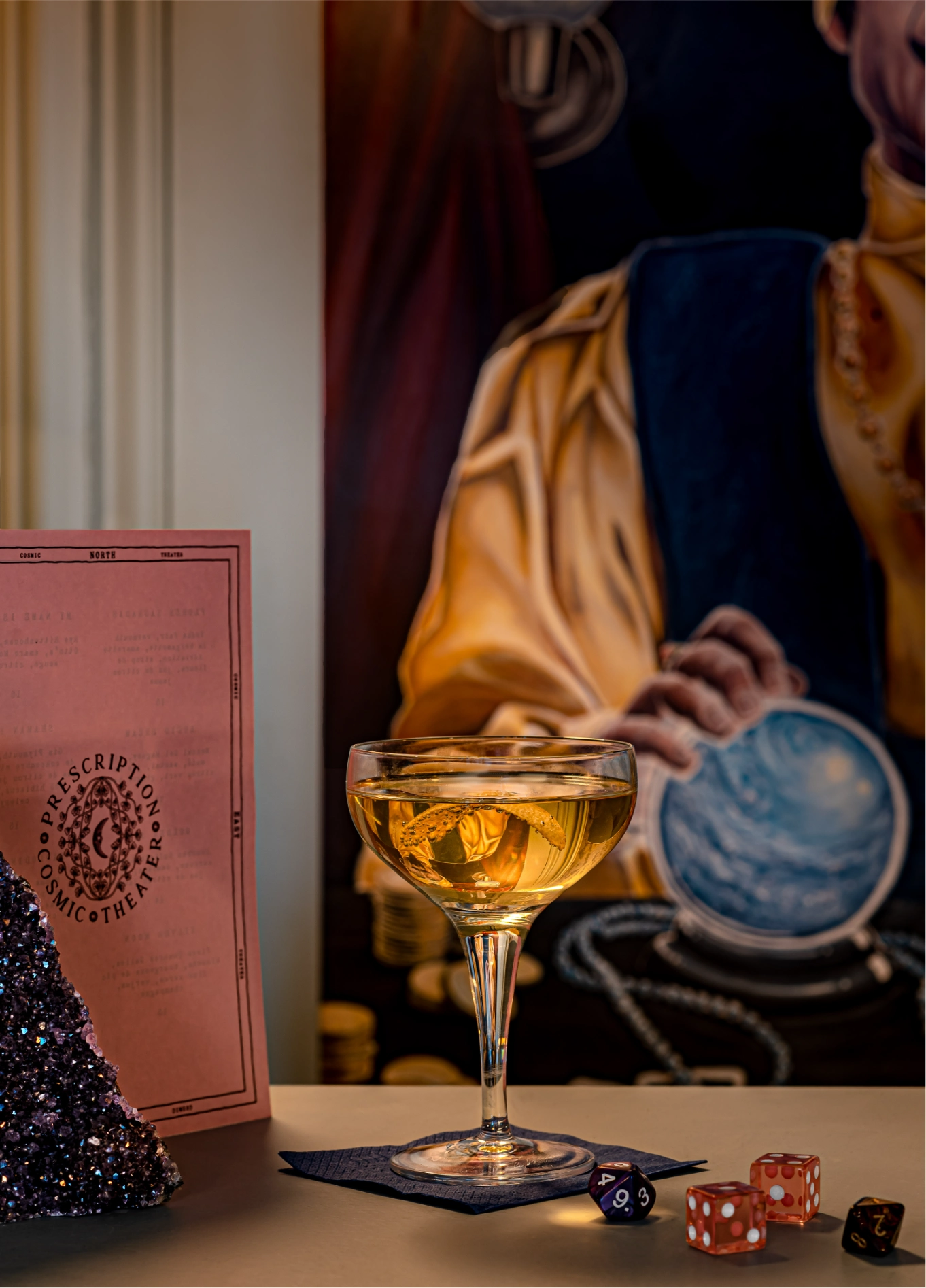 A cocktail served in a stemmed glass on a counter, with a pink menu and dice placed nearby.