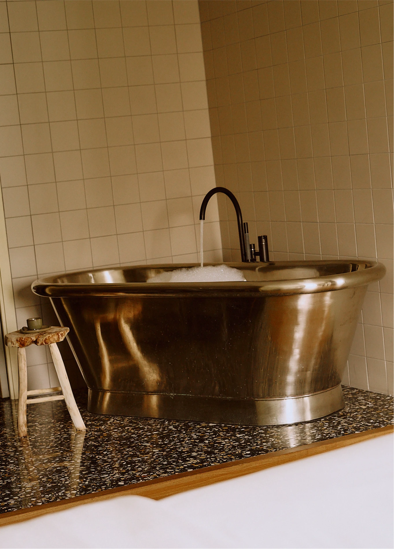 Modern bathtub on a dark terrazzo base, accompanied by a small wooden stool.