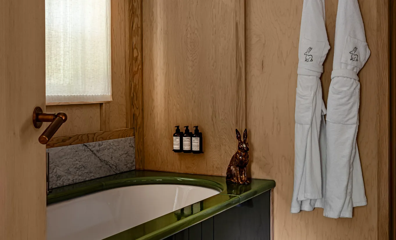 Bathroom with a green freestanding bathtub, wooden panelling and white bathrobes in the Grand Cowley Manor Suite at Cowley Manor Experimental, luxury retreat in the Cotswolds