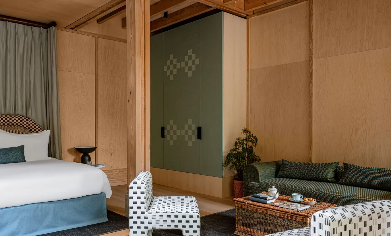 Bedroom with a white double bed, wooden wall panelling and a blue armchair in the Grand Cowley Manor Suite at Cowley Manor Experimental, a luxury spa hotel in the Cotswolds
