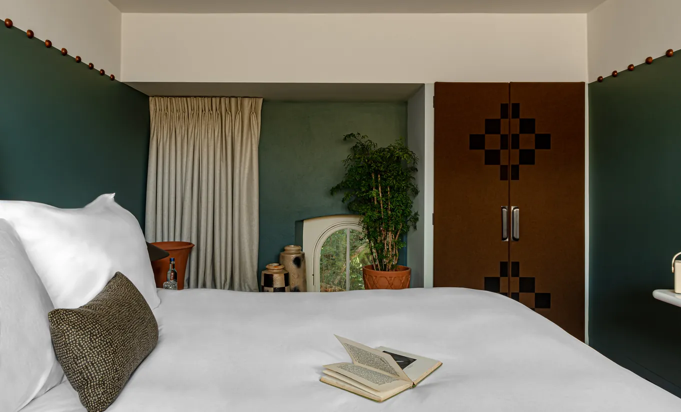 Bedroom with a white double bed, teal blue walls and a wooden door in the Treehouse room at Cowley Manor Experimental, Cotswolds