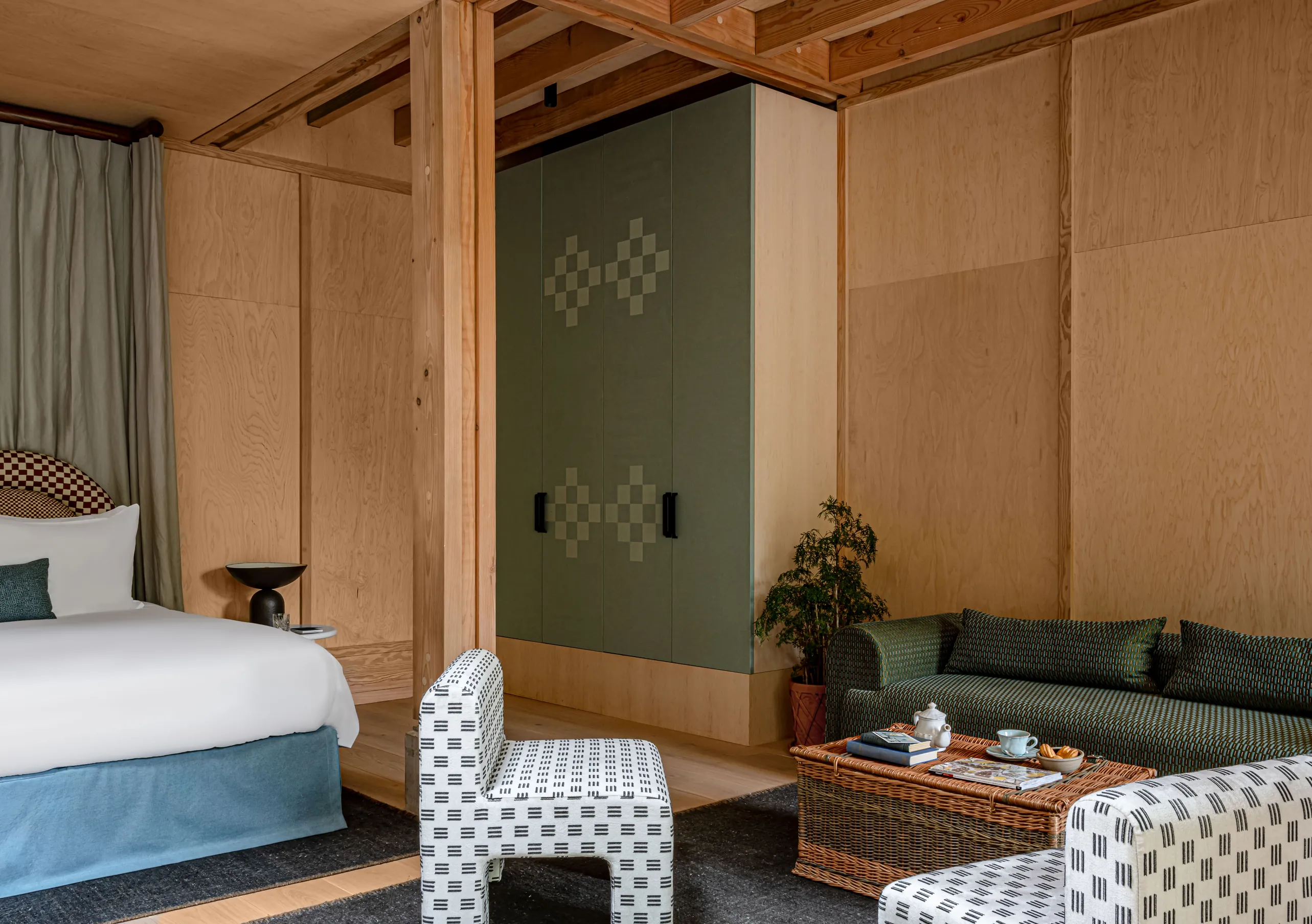 Bedroom with a white double bed, wooden wall panelling and a blue armchair in the Grand Cowley Manor Suite at Cowley Manor Experimental, a luxury spa hotel in the Cotswolds