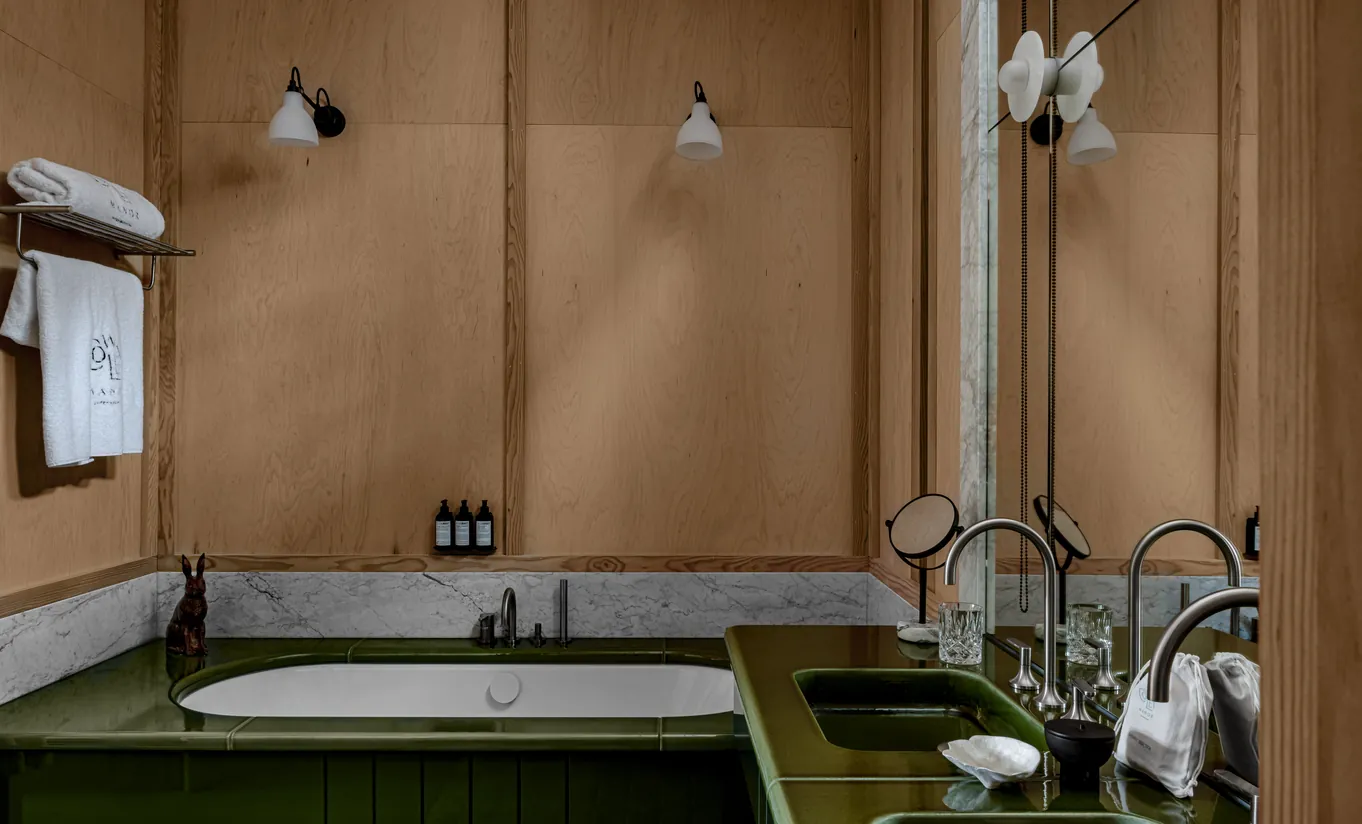 Bathroom with a green built-in bathtub, stone walls and vintage brass taps in the Waterlily with Terrace room at Cowley Manor Experimental, luxury spa hotel in the Cotswolds