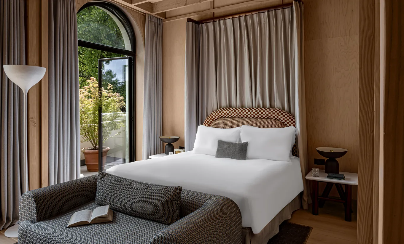 Bedroom with a white double bed, woven headboard and arched windows with linen curtains in the Waterlily with Terrace room at Cowley Manor Experimental, Cotswolds
