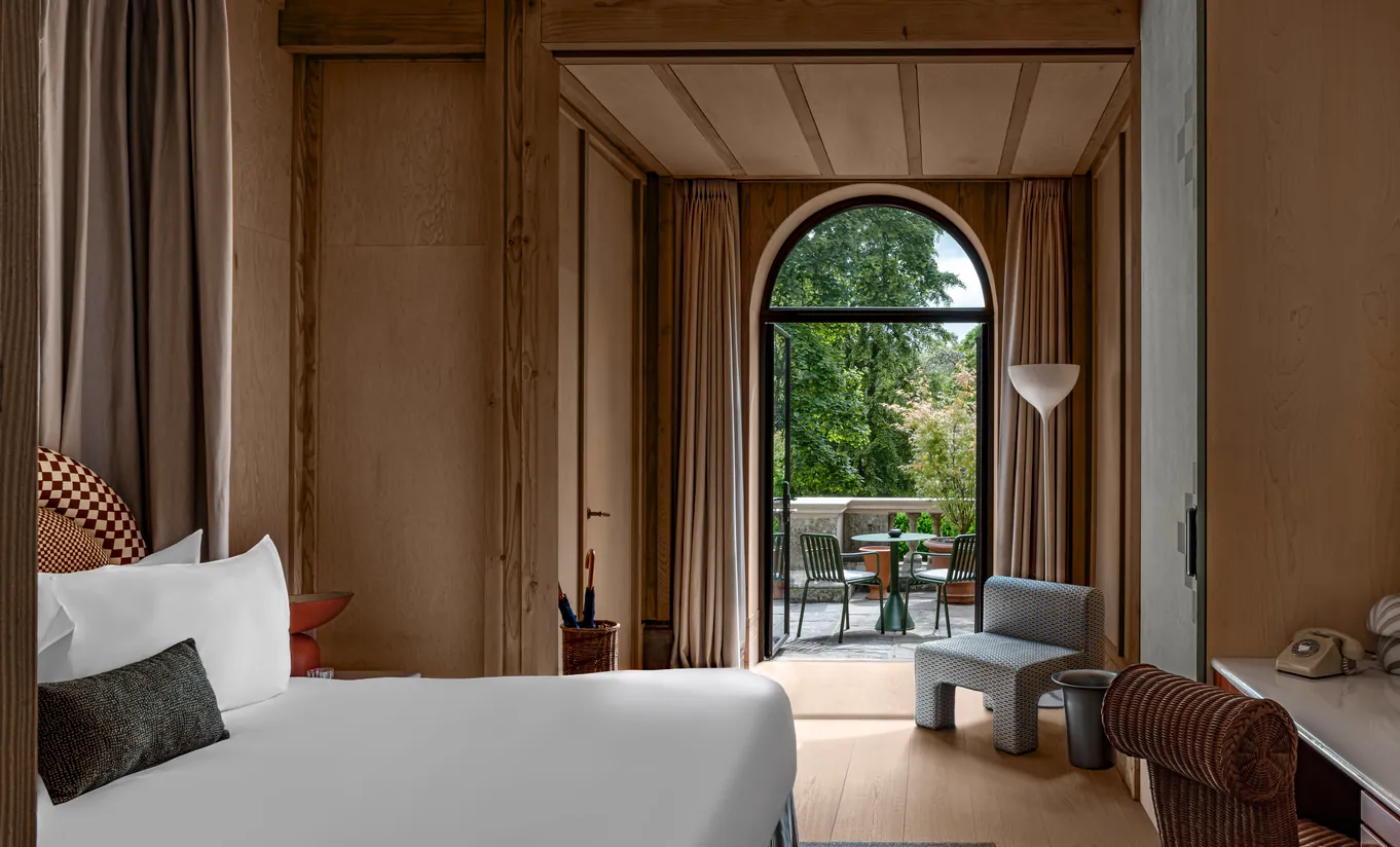 Bedroom with a white double bed and an arched door opening onto a private terrace with garden views in the Waterlily with Terrace room at Cowley Manor Experimental, Cotswolds