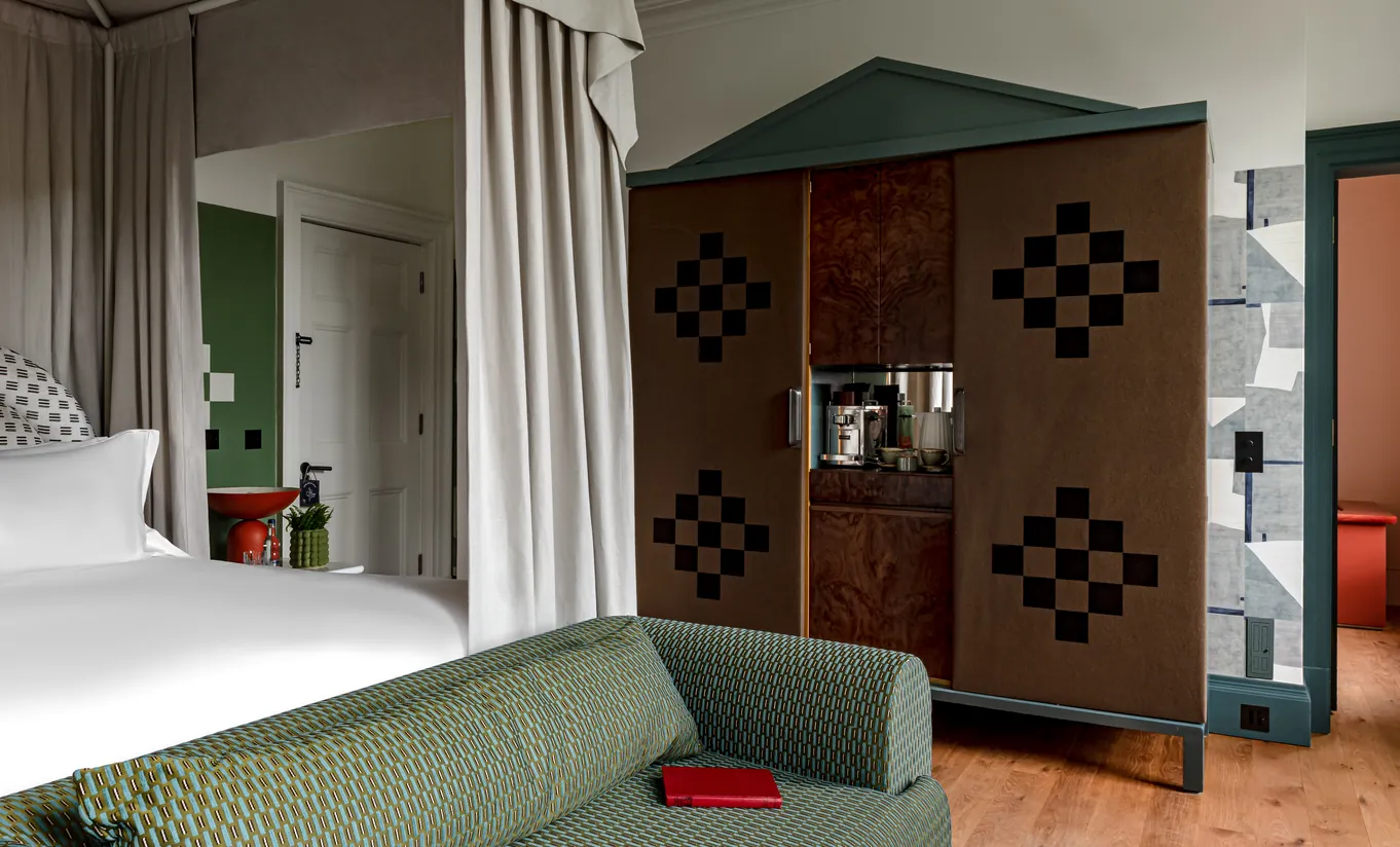 Bedroom with a white double bed, a checkered wardrobe and floor-length curtains in the Water Lily room at Cowley Manor Experimental, Cotswolds countryside retreat