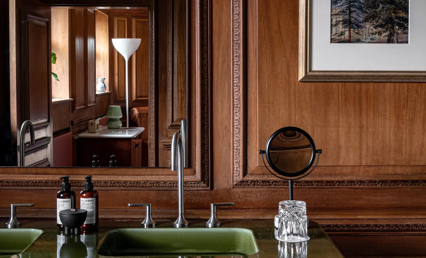 Bathroom with dark wood panelling, green double sinks and a vintage vanity mirror in the Water Lily room at Cowley Manor Experimental, Cotswolds