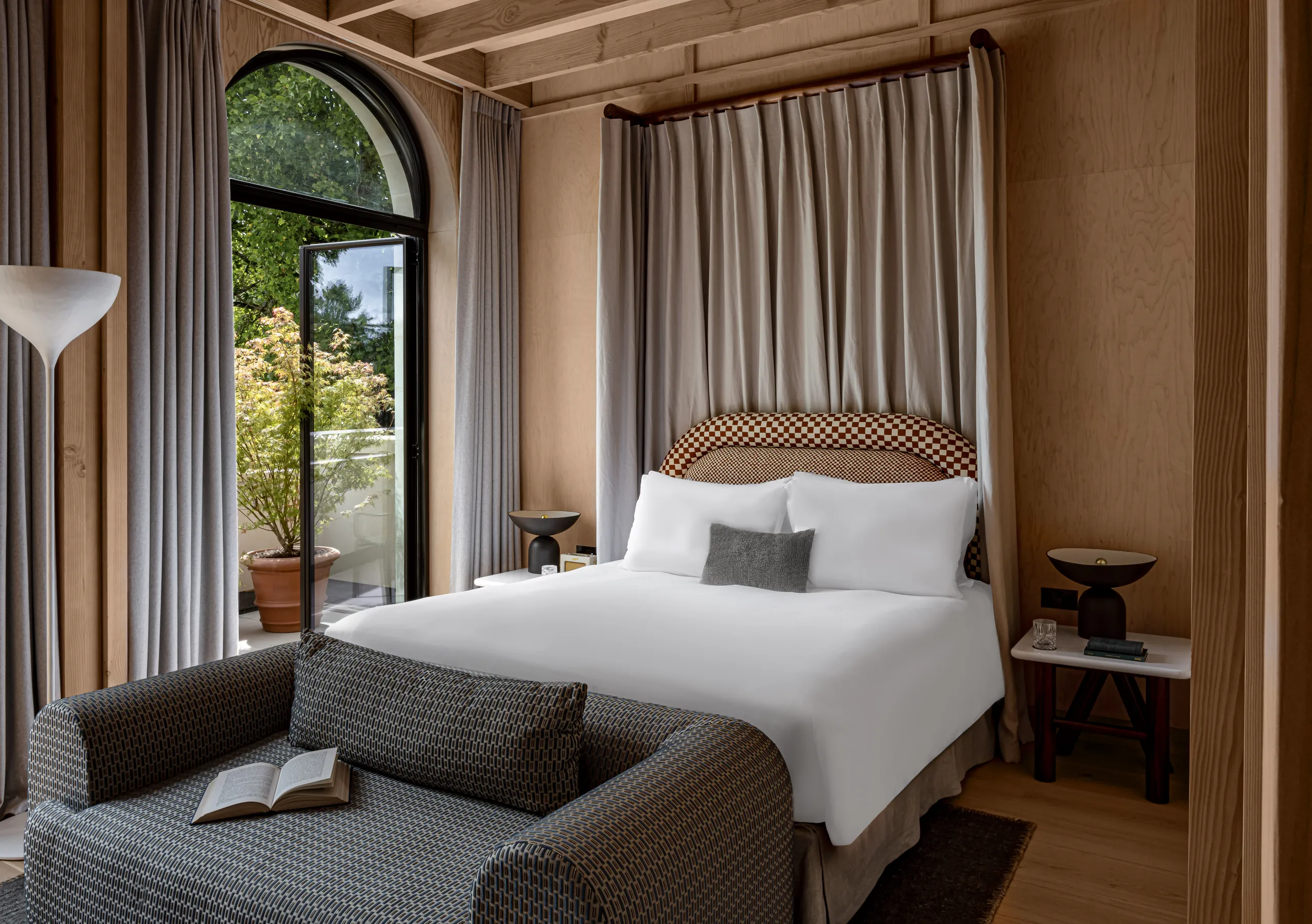 Bedroom with a white double bed, woven headboard and arched windows with linen curtains in the Waterlily with Terrace room at Cowley Manor Experimental, Cotswolds