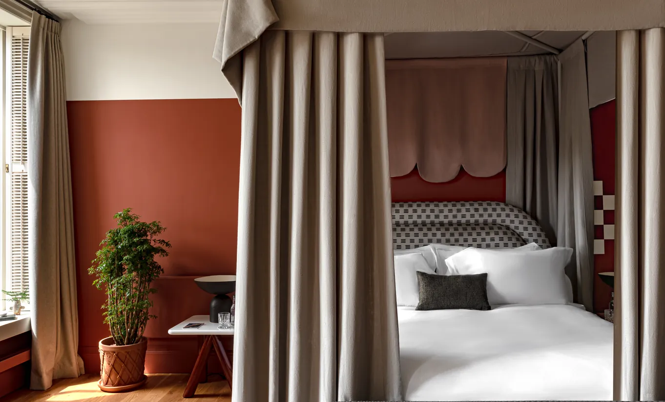 Bedroom with a four-poster bed, terracotta walls and floor-length linen curtains in the Swan Lake Suite at Cowley Manor Experimental, a luxury countryside retreat in the Cotswolds