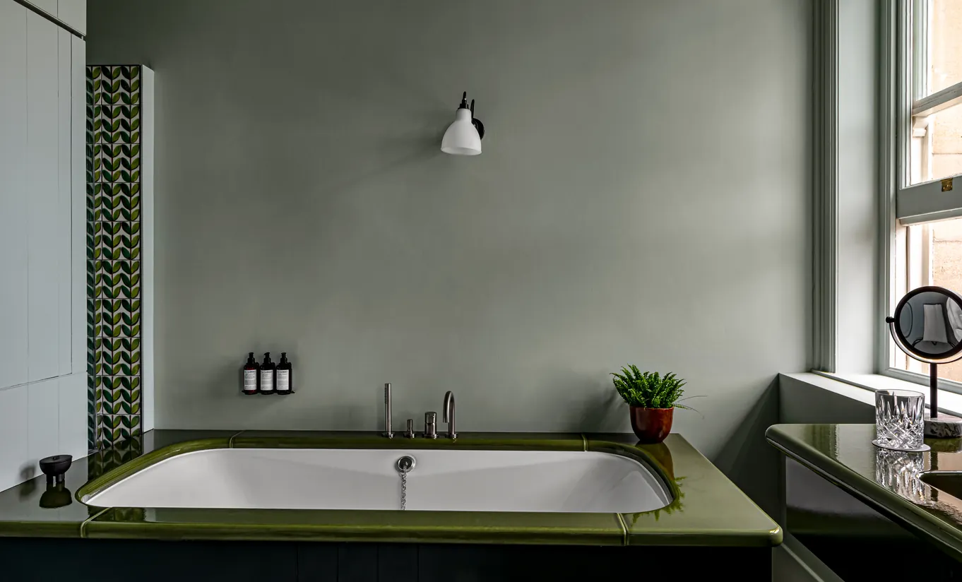 Bathroom with a built-in green bathtub, sage green walls and warm lighting in the Swan Lake Suite at Cowley Manor Experimental, luxury spa hotel in the Cotswolds