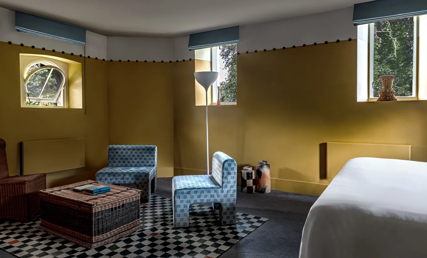Sitting area with a daybed, checkered floor and mustard yellow walls in the Wildflower room at Cowley Manor Experimental, countryside retreat in the Cotswolds