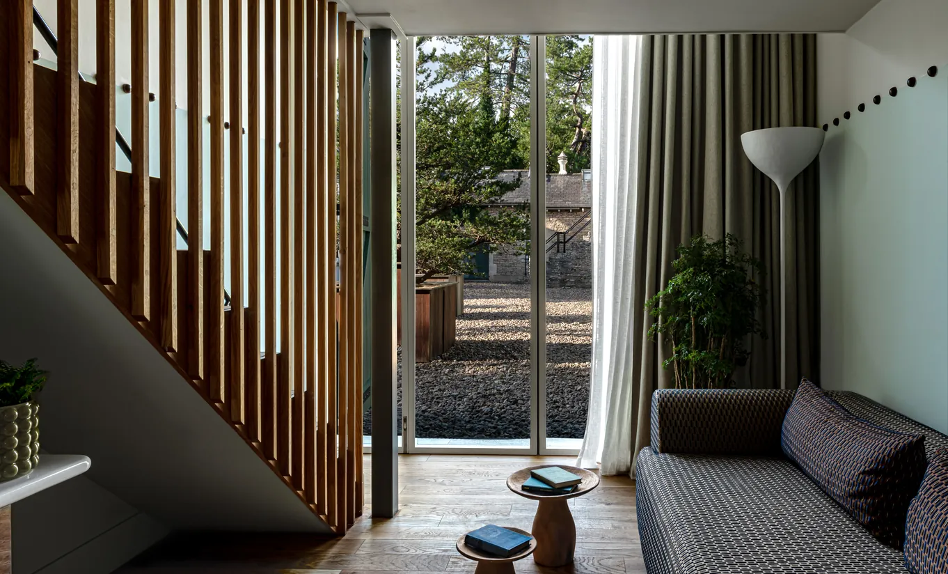 Bright living area with slatted wooden partitions, a sofa and large windows overlooking the grounds in the Treehouse room at Cowley Manor Experimental, Cotswolds