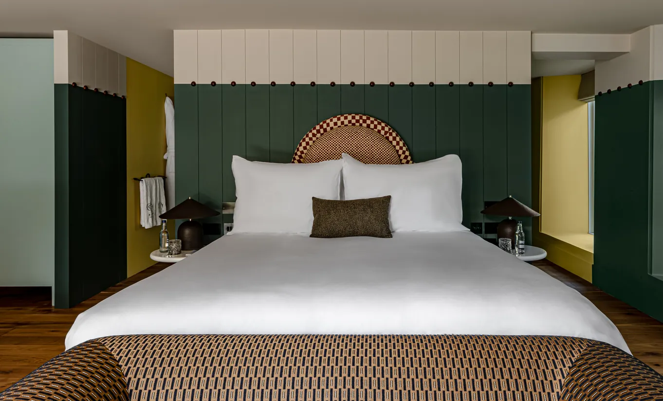 Bedroom with a king-size bed, mustard yellow walls, dark green panelling and a rattan headboard in the Wildflower with Terrace room at Cowley Manor Experimental, Cotswolds