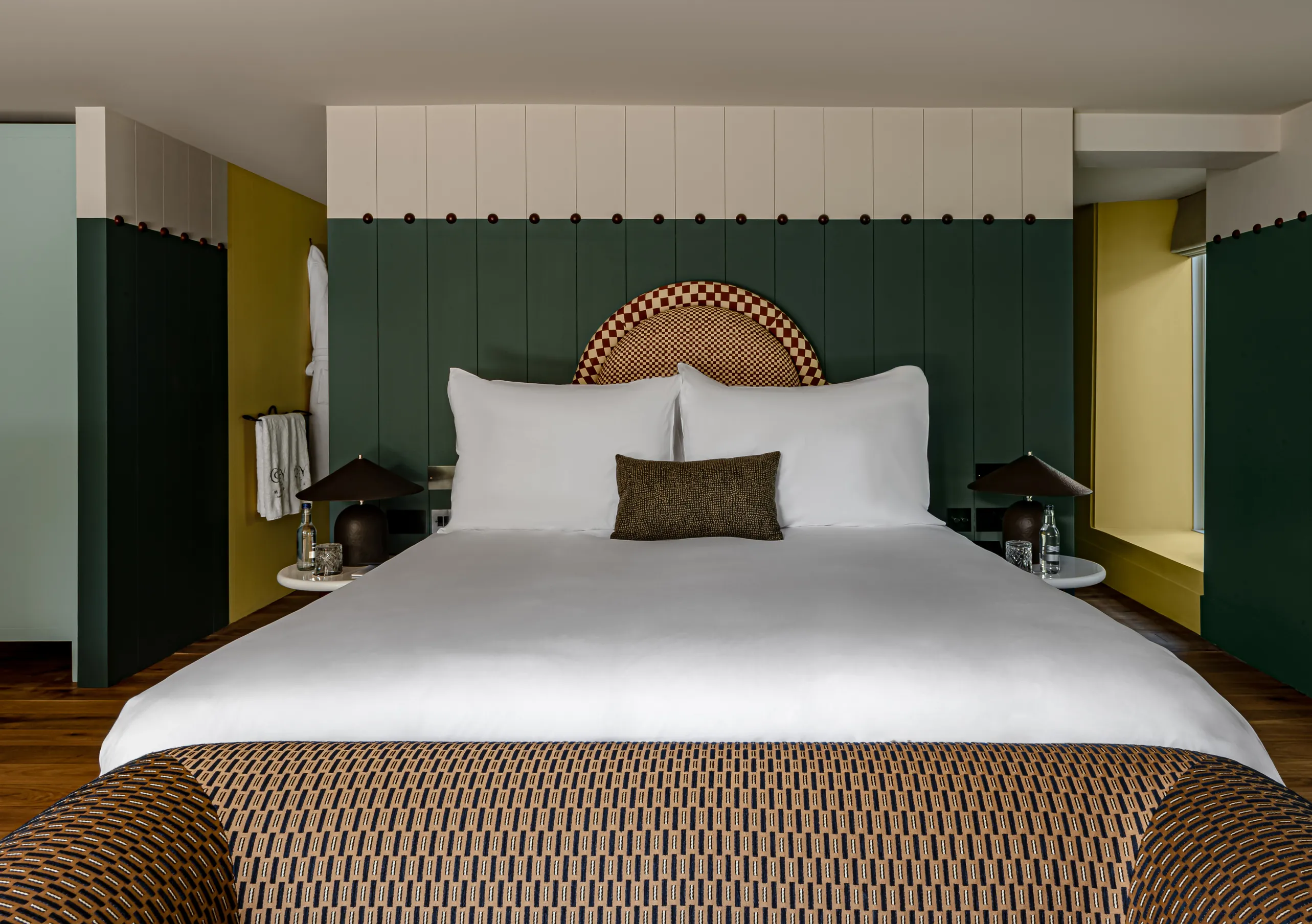 Bedroom with a king-size bed, mustard yellow walls, dark green panelling and a rattan headboard in the Wildflower with Terrace room at Cowley Manor Experimental, Cotswolds.