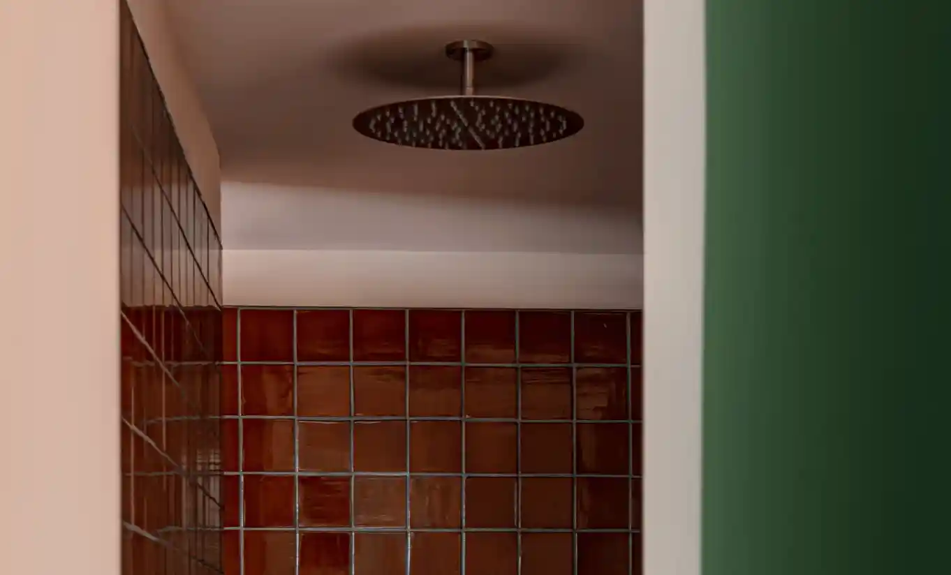 Shower with a rain showerhead and dark red square tiles in the Churns River Junior Suite at Cowley Manor Experimental, Cotswolds
