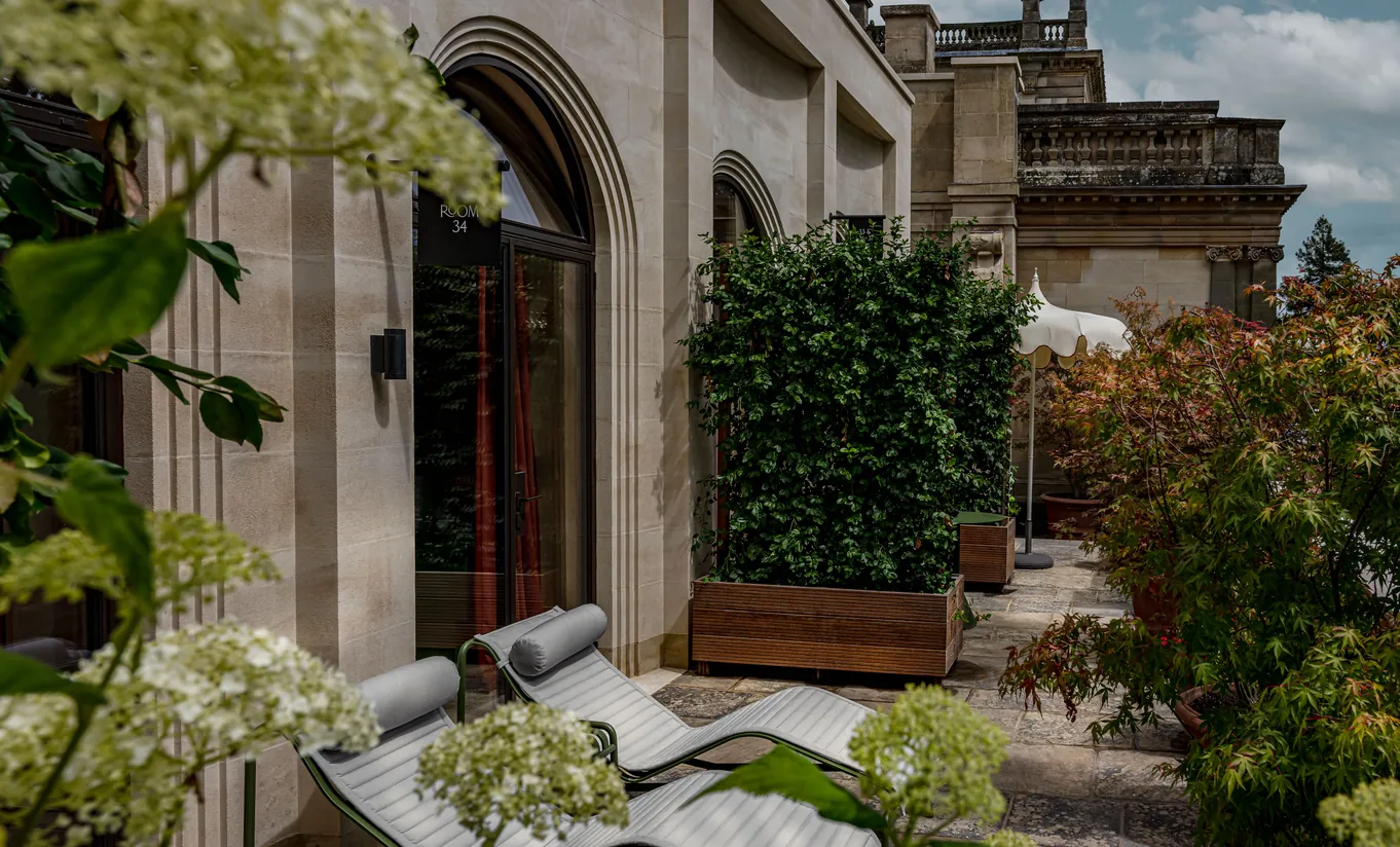 Exterior view of the stone manor facade with a private terrace and garden furniture surrounded by hydrangeas at Cowley Manor Experimental, Cotswolds