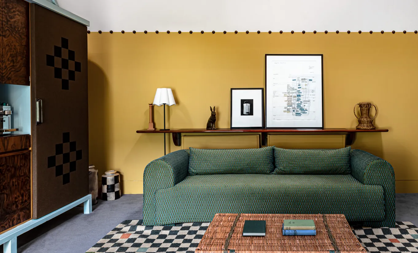 Living area with a green sofa, mustard yellow walls and a geometric patterned rug in the Churns River Junior Suite at Cowley Manor Experimental, luxury hotel in the Cotswolds