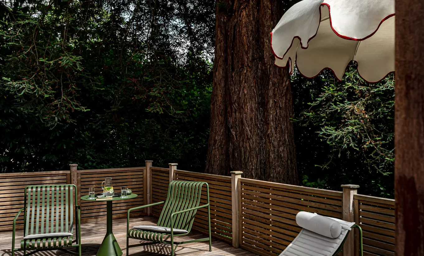 Private wooden terrace with garden chairs surrounded by tall trees in the Wildflower with Terrace room at Cowley Manor Experimental, ideal for a relaxing countryside escape in the Cotswolds