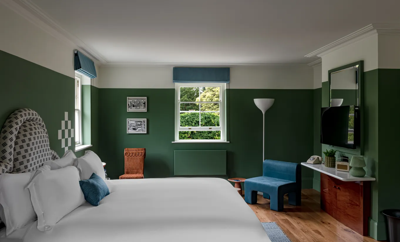 Bedroom with a white double bed, deep green walls and a blue bench at the foot of the bed in the Churns River Junior Suite at Cowley Manor Experimental, Cotswolds