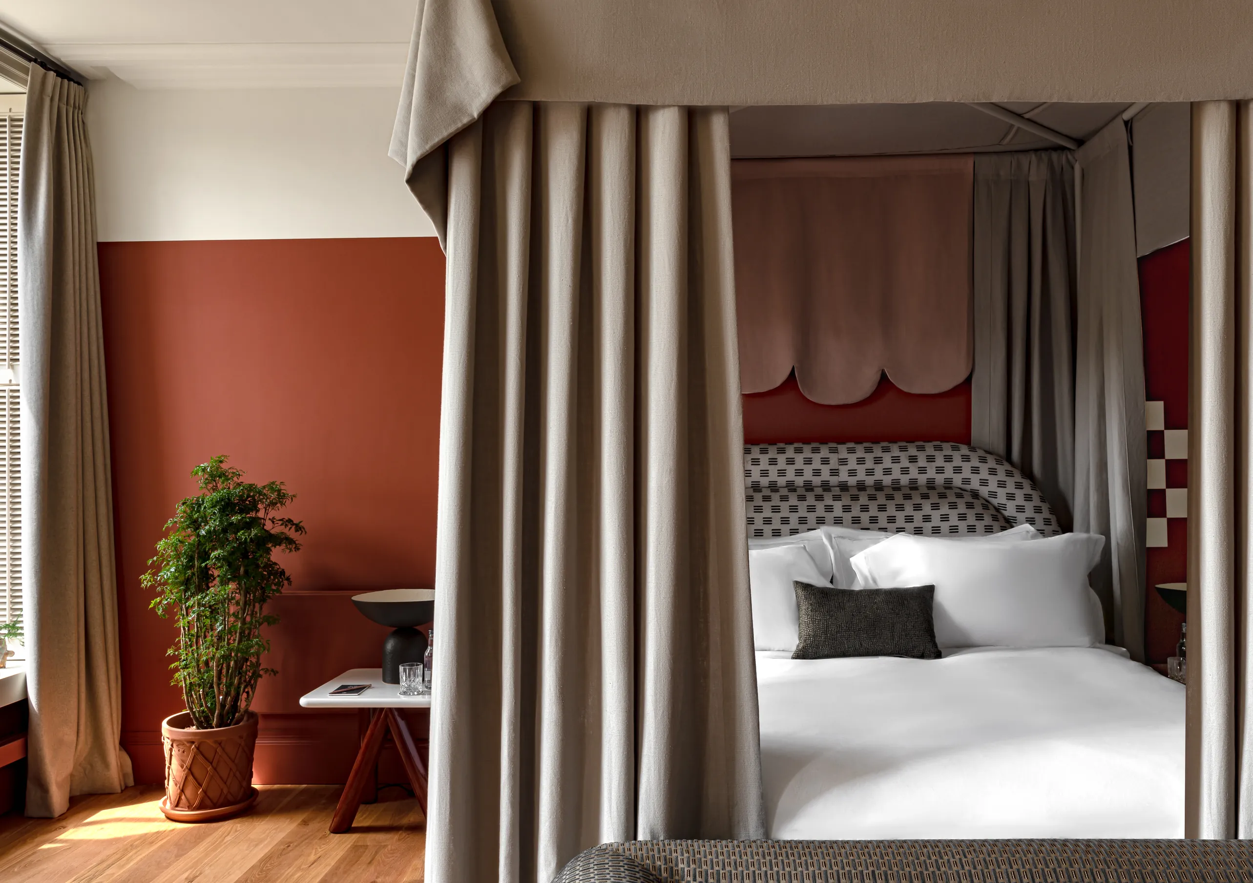 Bedroom with a four-poster bed, terracotta walls and floor-length linen curtains in the Swan Lake Suite at Cowley Manor Experimental, a luxury countryside retreat in the Cotswolds