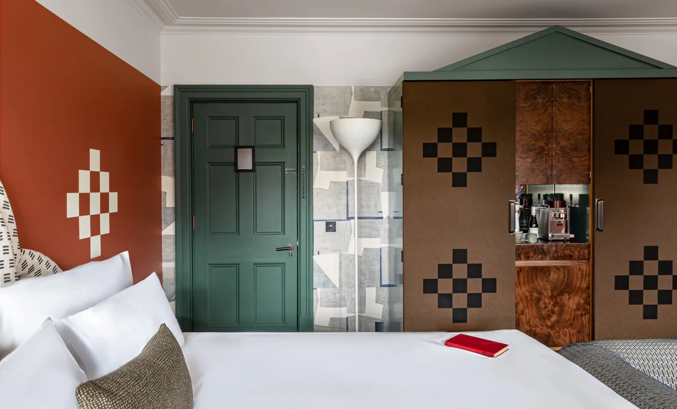Bedroom with a white double bed, terracotta walls, a dark green door and a checkered wardrobe in the Petite Cowley room at Cowley Manor Experimental, Cotswolds