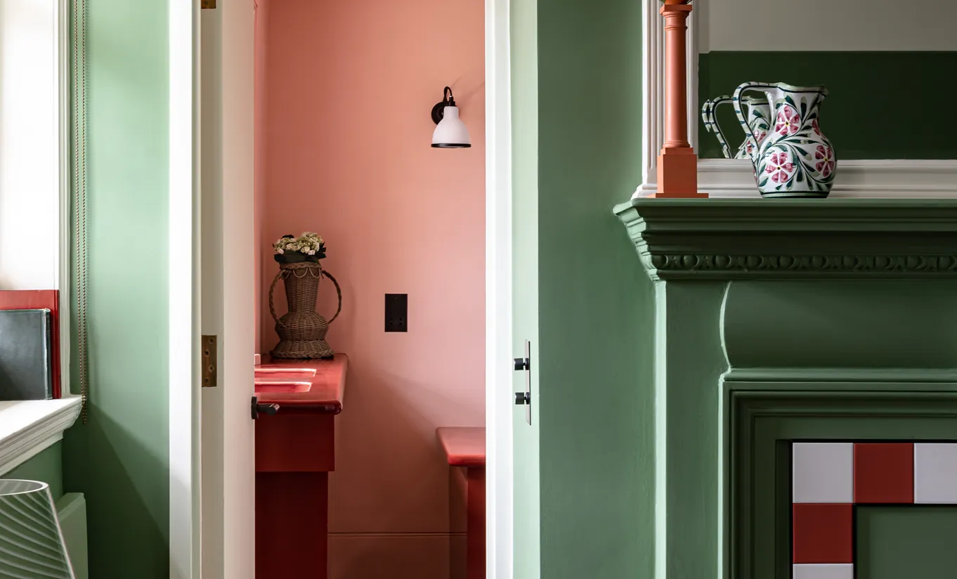 Detail of a bedroom corner with sage green woodwork, a red and white tiled fireplace and terracotta walls in the Petite Cowley room at Cowley Manor Experimental, Cotswolds