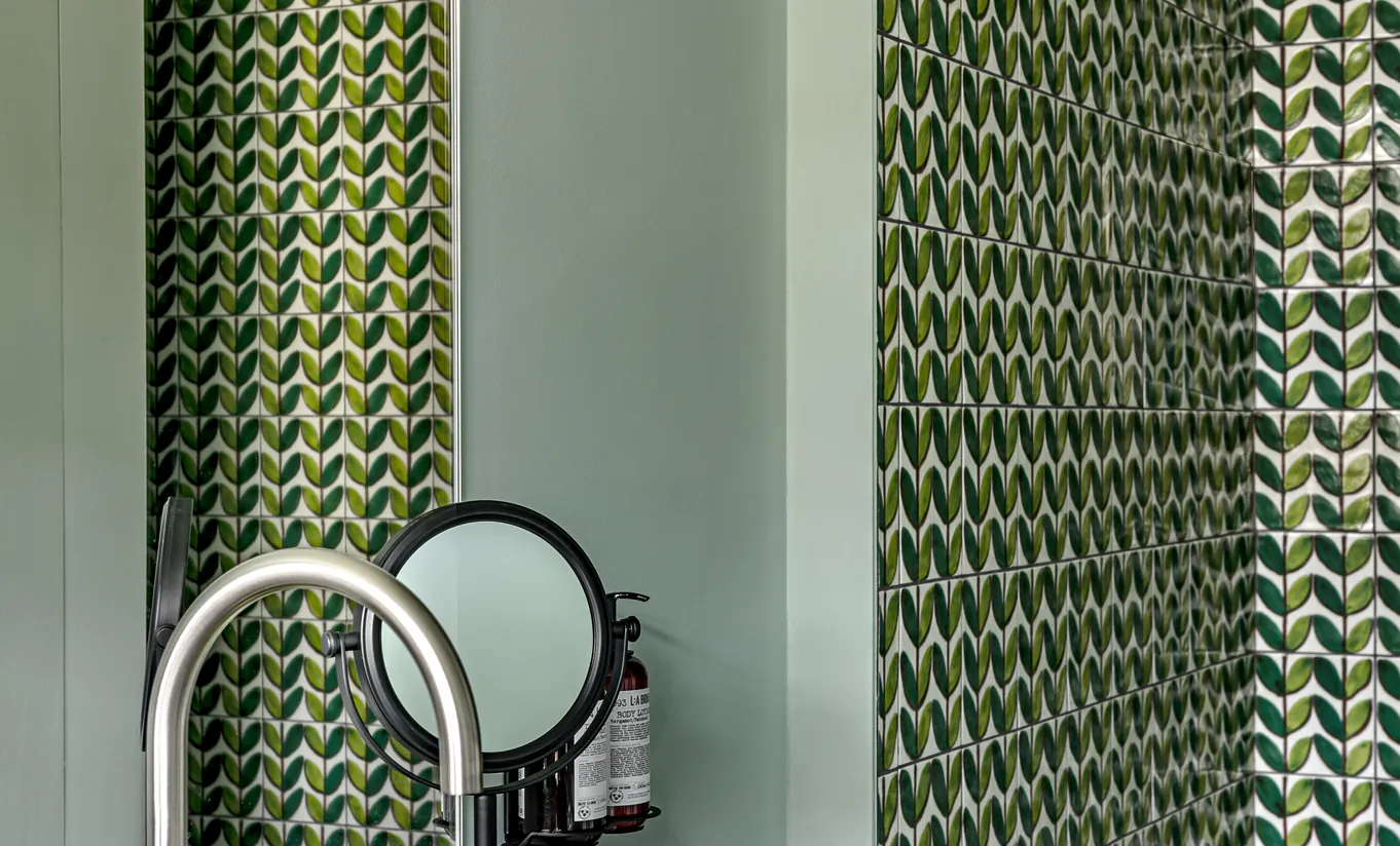 Bathroom with green herringbone tiled walls, a round mirror and brass fixtures in the Petite Cowley room at Cowley Manor Experimental, luxury hotel in the Cotswolds