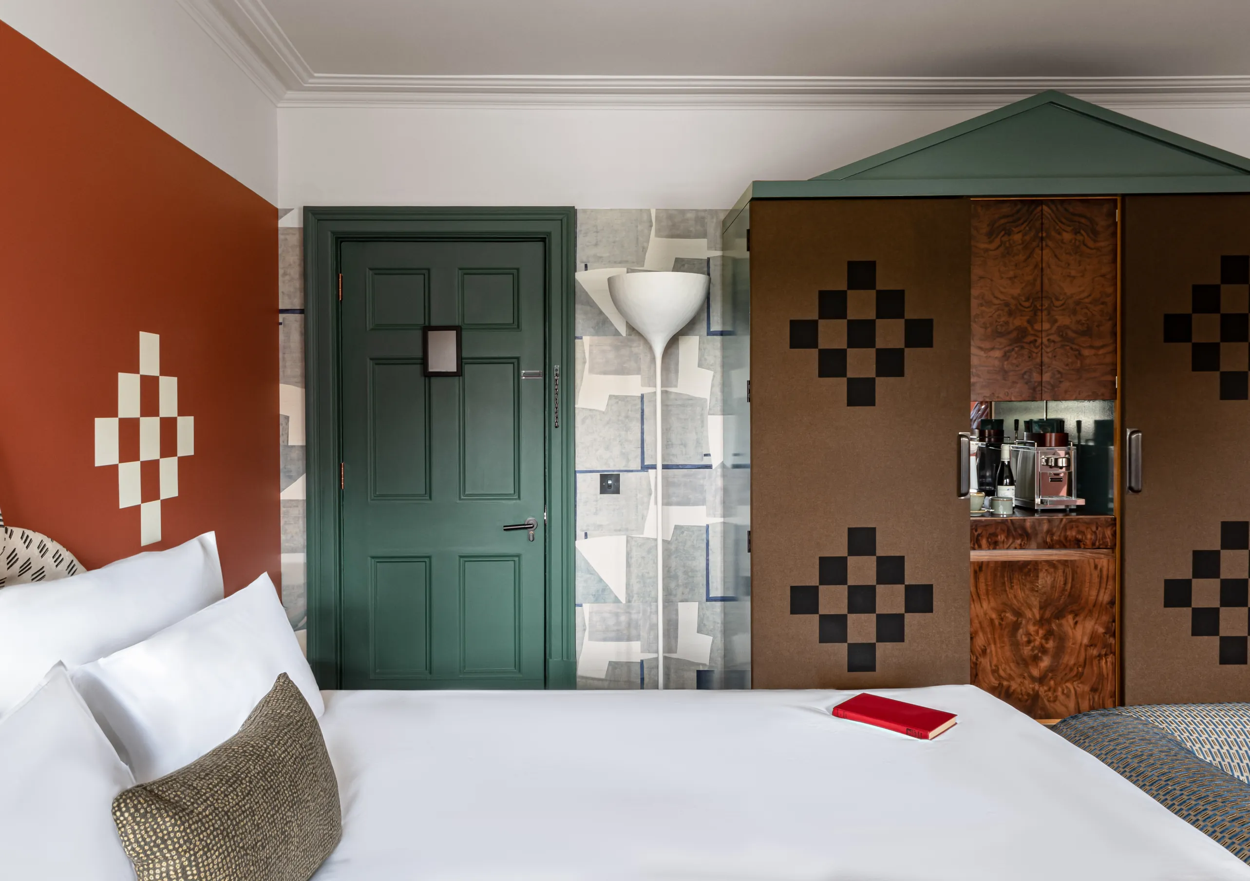 Bedroom with a white double bed, terracotta walls, a dark green door and a checkered wardrobe in the Petite Cowley room at Cowley Manor Experimental, Cotswolds