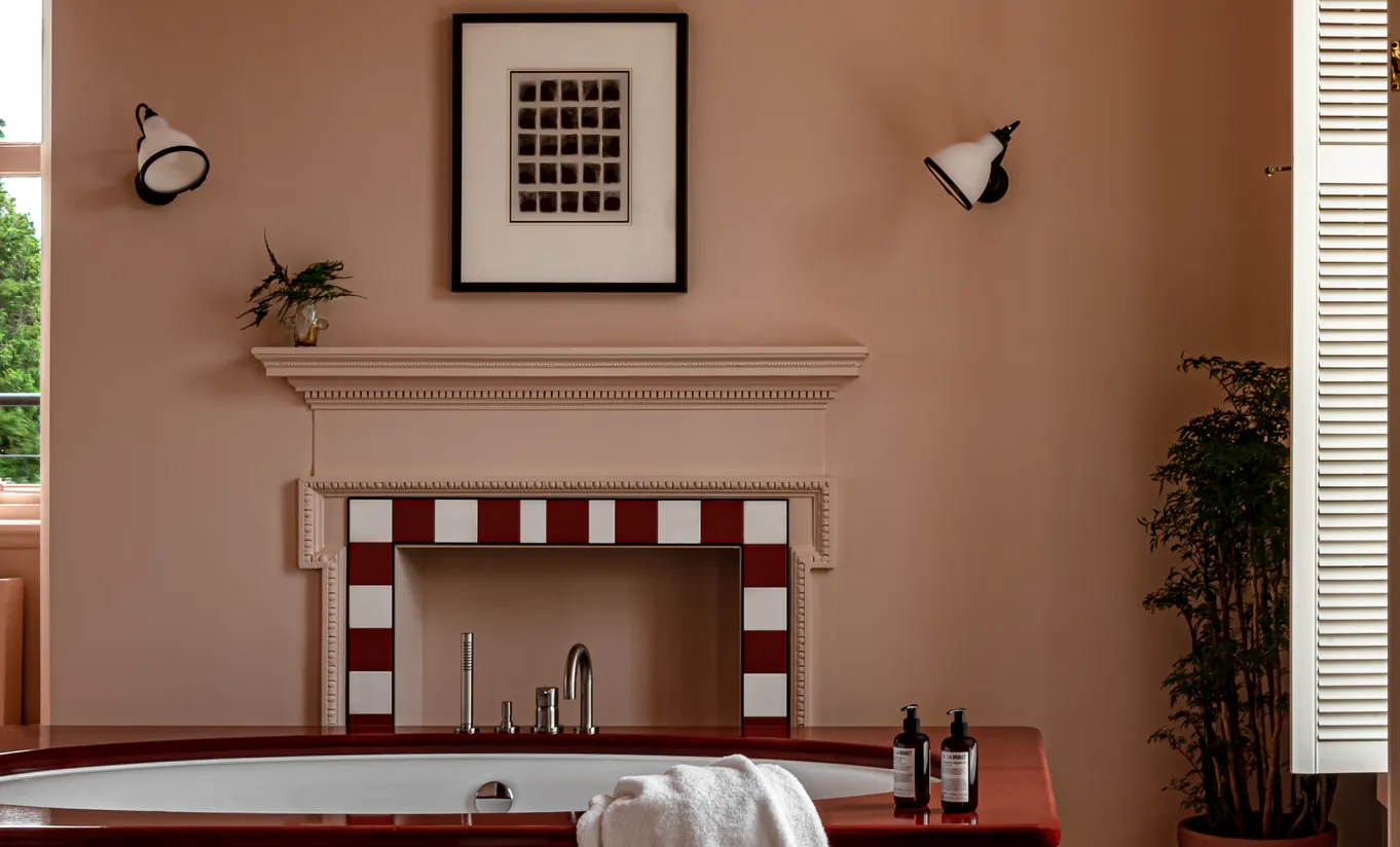 Bathroom with a red and white tiled fireplace, terracotta walls and a freestanding bathtub in the Cowley Manor Suite at Cowley Manor Experimental, Cotswolds