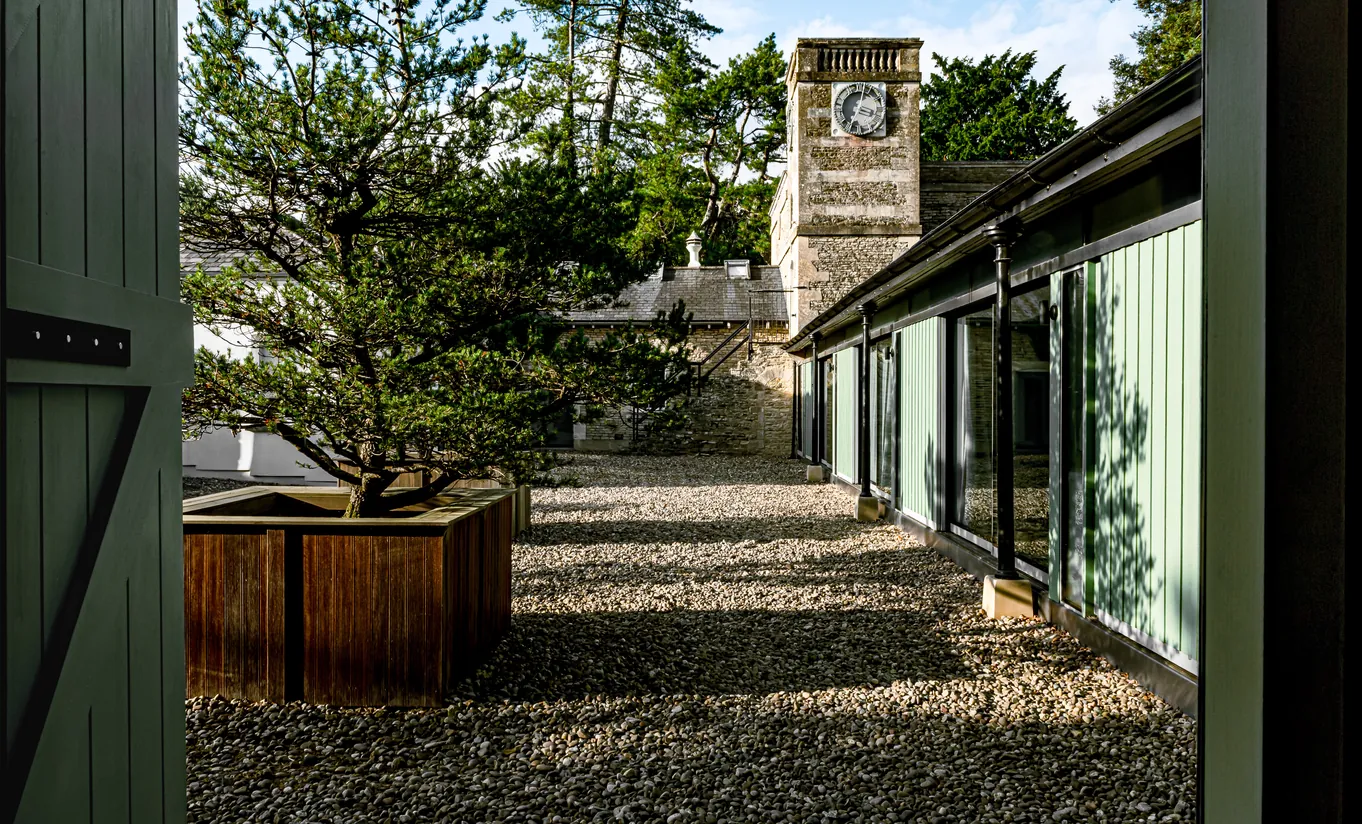 Exterior walkway with a bonsai tree and pebbled path leading to the Treehouse room at Cowley Manor Experimental, unique countryside retreat in the Cotswolds