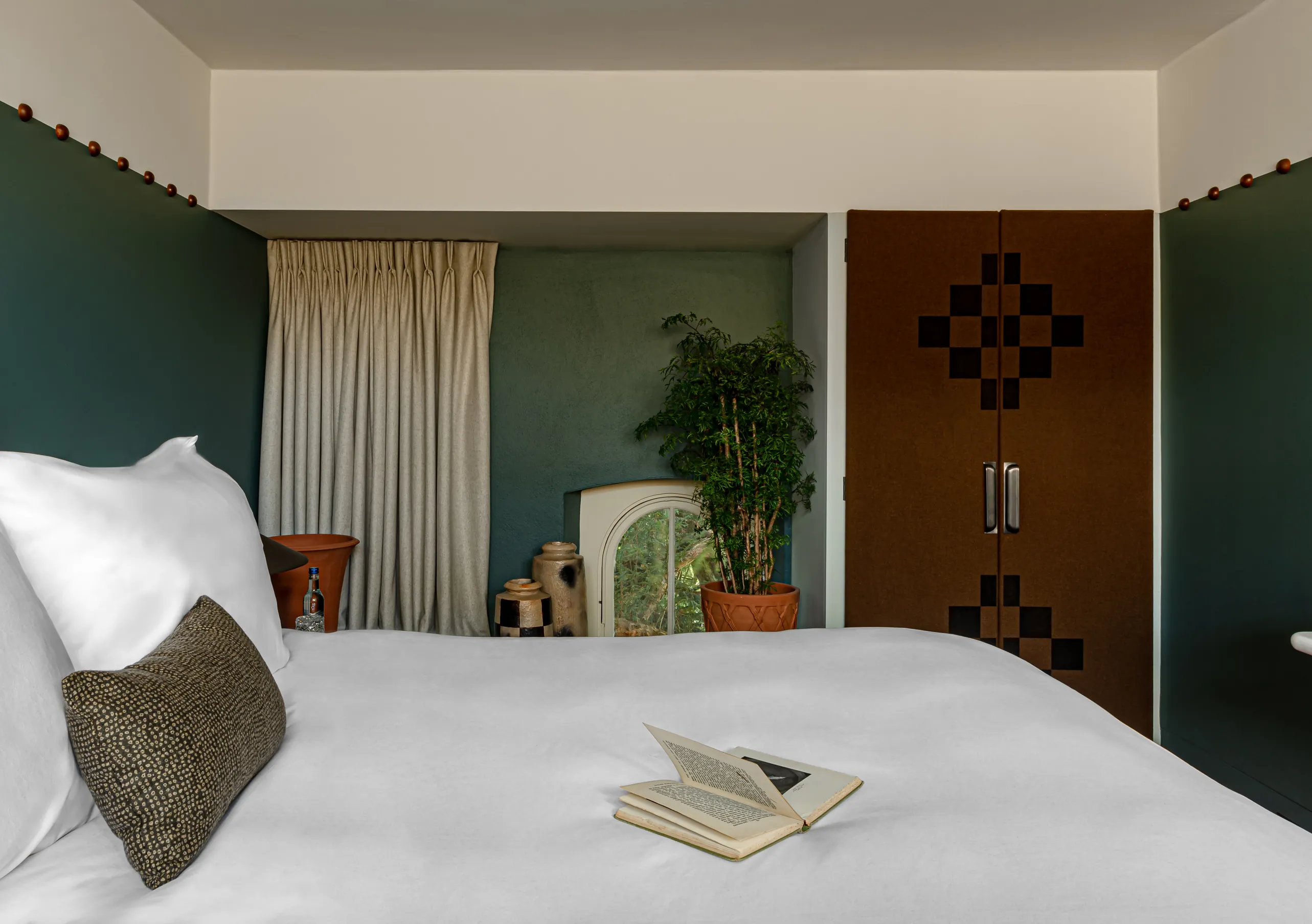 Bedroom with a white double bed, teal blue walls and a wooden door in the Treehouse room at Cowley Manor Experimental, Cotswolds
