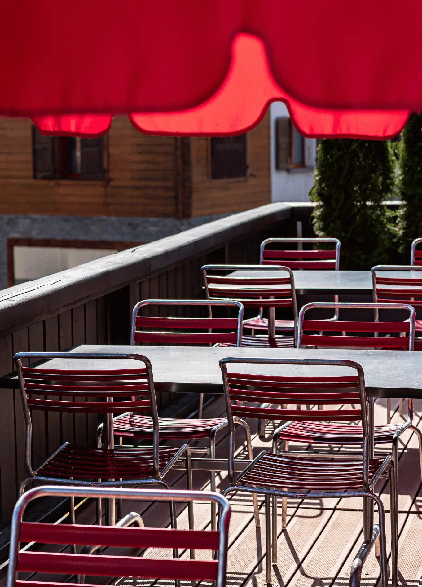Outdoor terrace with red metal chairs and tables under a red parasol at Experimental Chalet Verbier, luxury spa hotel in the Swiss Alps