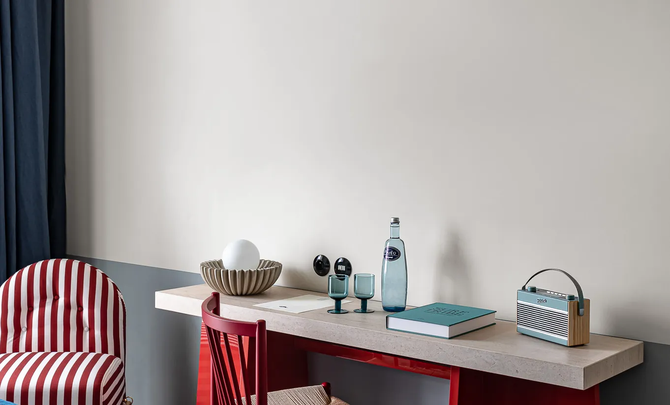 Regina Experimental hotel desk area with red chair, blue water bottle and minimalist white wall in Venice