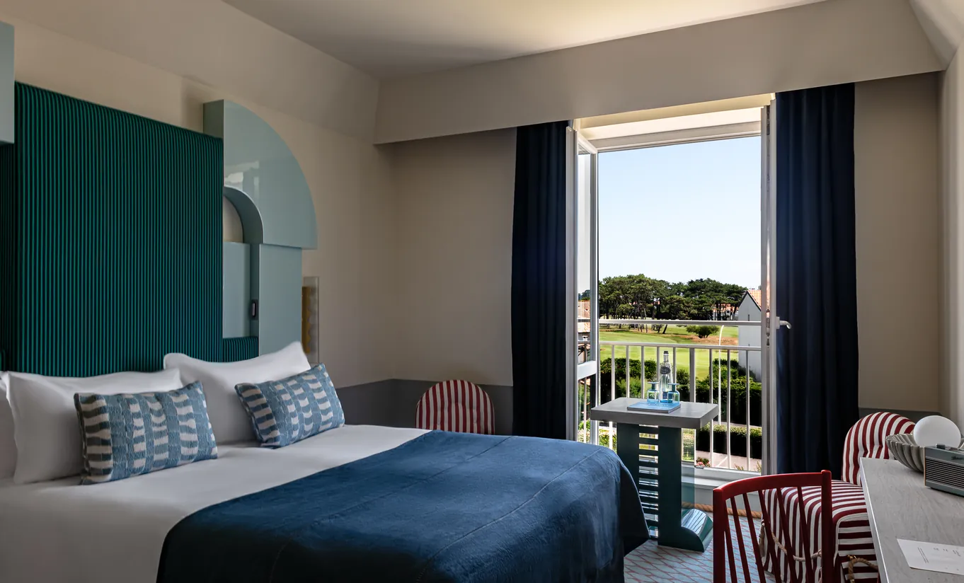 Bright hotel room with teal upholstered headboard, white linen bedding and panoramic garden view at Experimental Group.